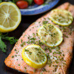 Baked Steelhead Trout Fillet with three sliced lemons sprinkled with a green herb