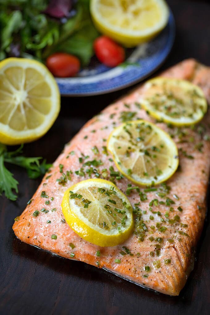 Baked Steelhead Trout with 3 lemon slices sprinkled with green herb on a wood board