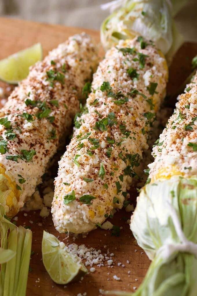 Three Mexican Street Corn (Elotes) on wooden board with lime wedges