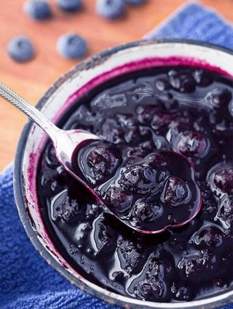 Blueberry Compote being spooned out of small bowl with silver spoon