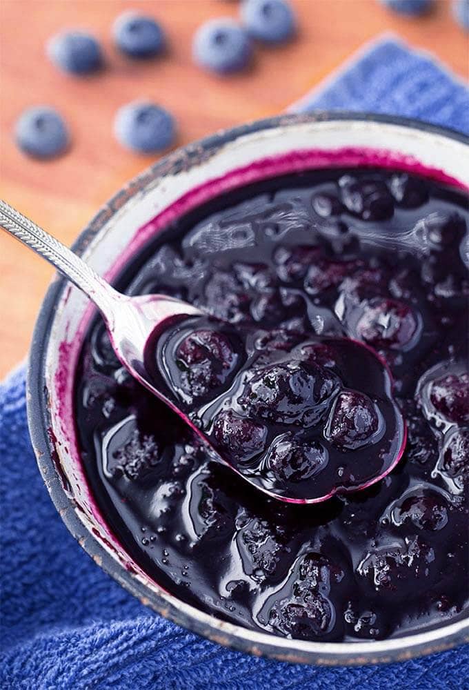 Blueberry Compote being spooned out of small bowl with silver spoon