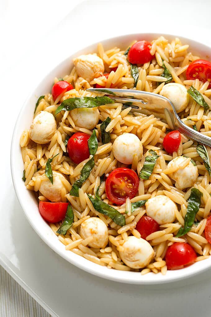 Caprese Orzo Salad with fork in a bowl on a white plate