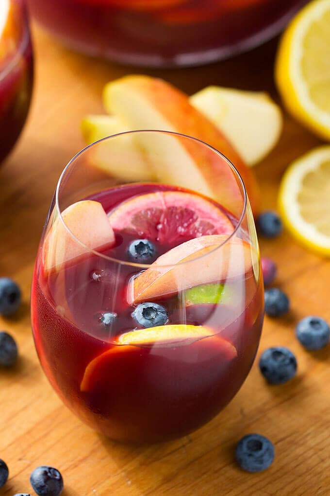 Fruity Red Sangria in a glass on a wooden board surrounded by blueberries, lemon slices, and apple slices