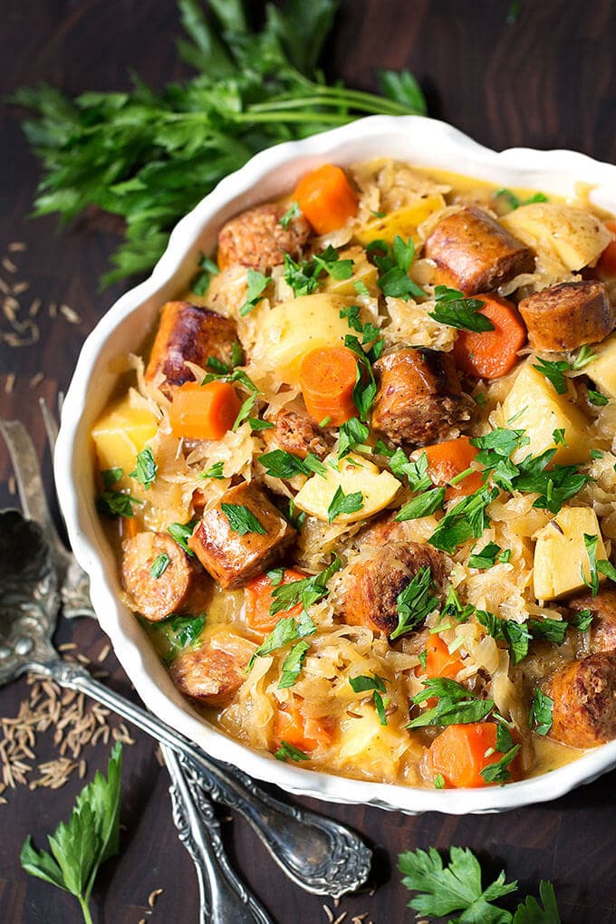 Instant Pot Kielbasa and Sauerkraut garnished with parsley in white bowl with silver spoon and fork at the side 