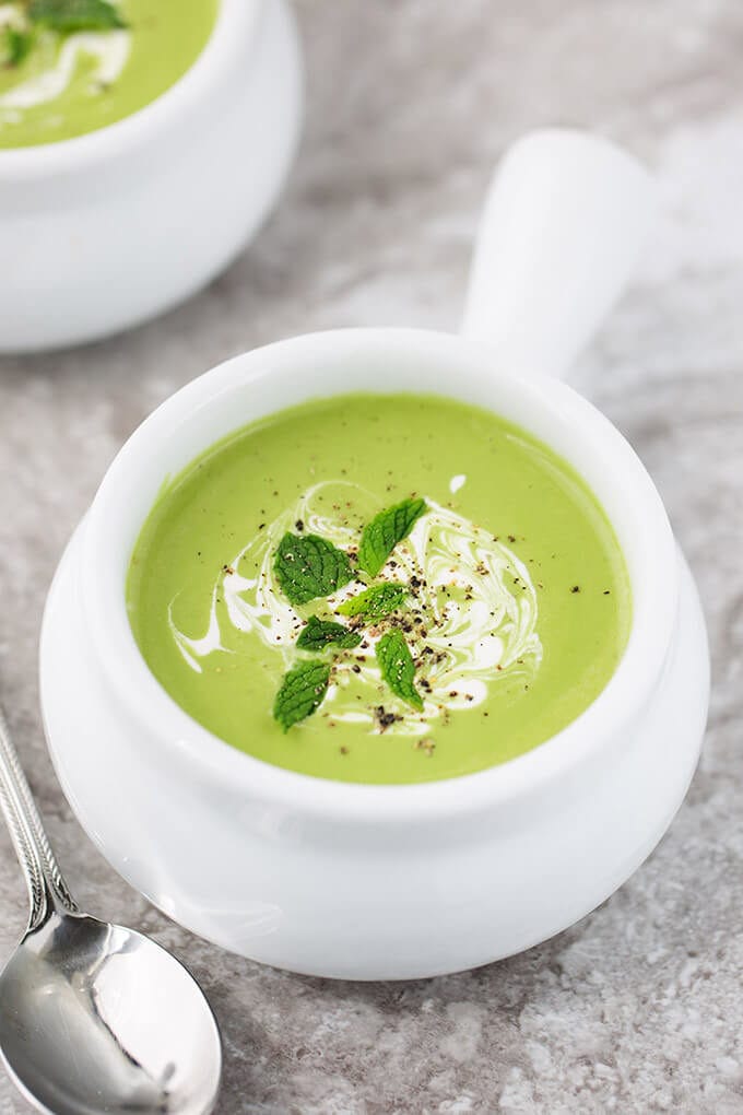 Minty Pea Soup in small white bowl with handle with a silver spoon on a grey stone background
