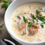 Pacific Oyster Stew in white bowl on wooden board with silver spoon