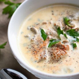 Pacific Oyster Stew in white bowl on wooden board with silver spoon