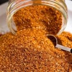 Ribs Spice Rub spilling out of a small glass jar with a measuring spoon scooping spice