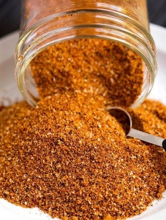 Ribs Spice Rub spilling out of a small glass jar with a measuring spoon scooping spice