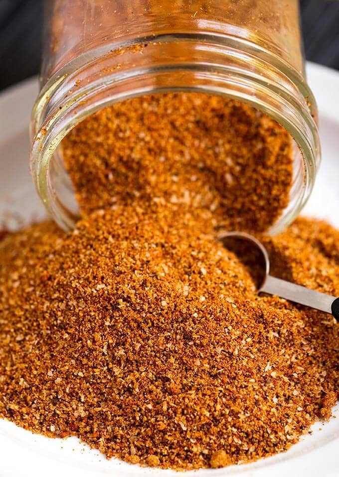 Ribs Spice Rub spilling out of a small glass jar with a measuring spoon scooping spice