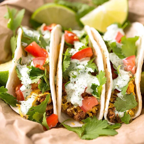 Three Turkey Street Tacos With Cilantro Cream Sauce on brown paper garnished with cilantro and lime wedges