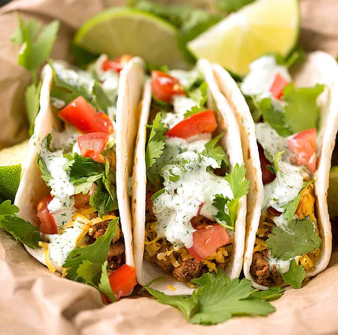 Close up of three Turkey Street Tacos With Cilantro Cream Sauce on brown paper garnished with cilantro