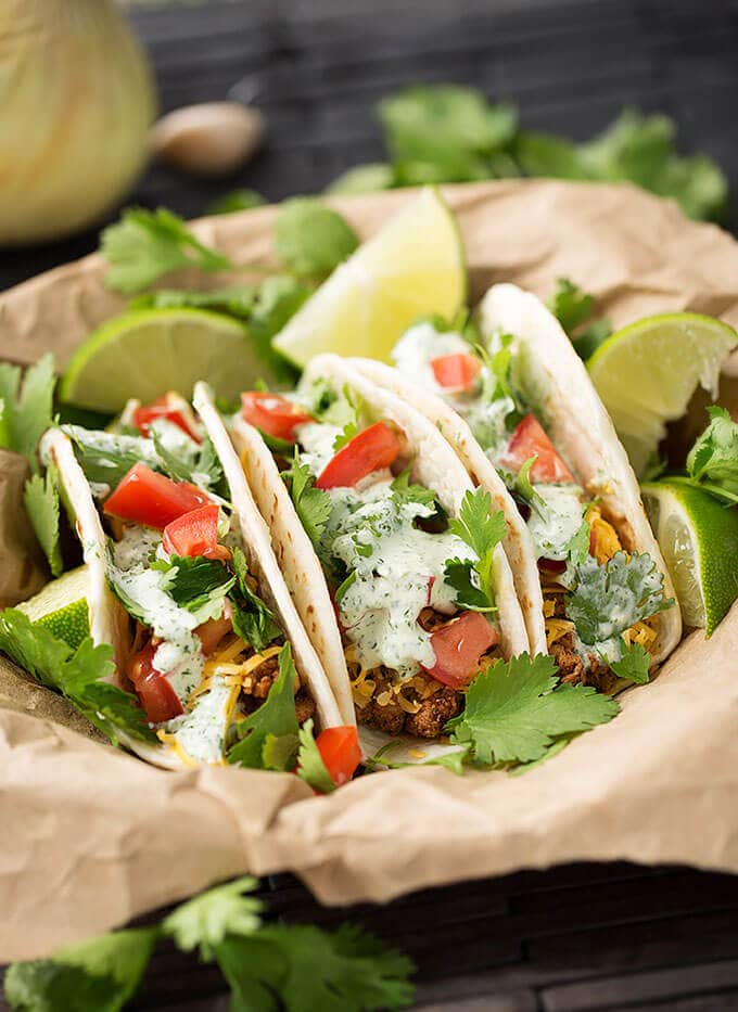 Three Turkey Street Tacos With Cilantro Cream Sauce on brown paper and garnished with cilantro and lime wedges