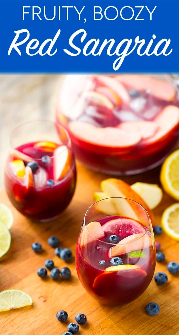 Fruity Red Sangria in a stemless wine glass with a pitcher behind it