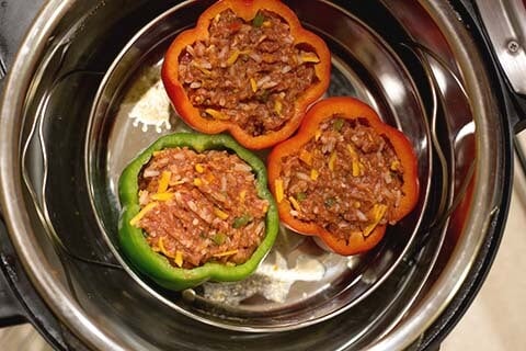 Three uncooked stuffed peppers in a metal pan in a pressure cooker