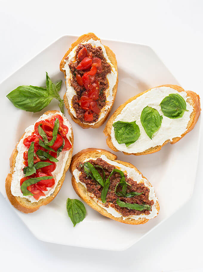 Four Bruschetta on a white plate with fresh basil