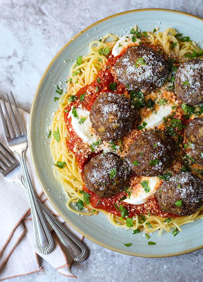 Easy Baked Meatballs topping spaghetti and marinara sauce on a light blue plate next to two forks