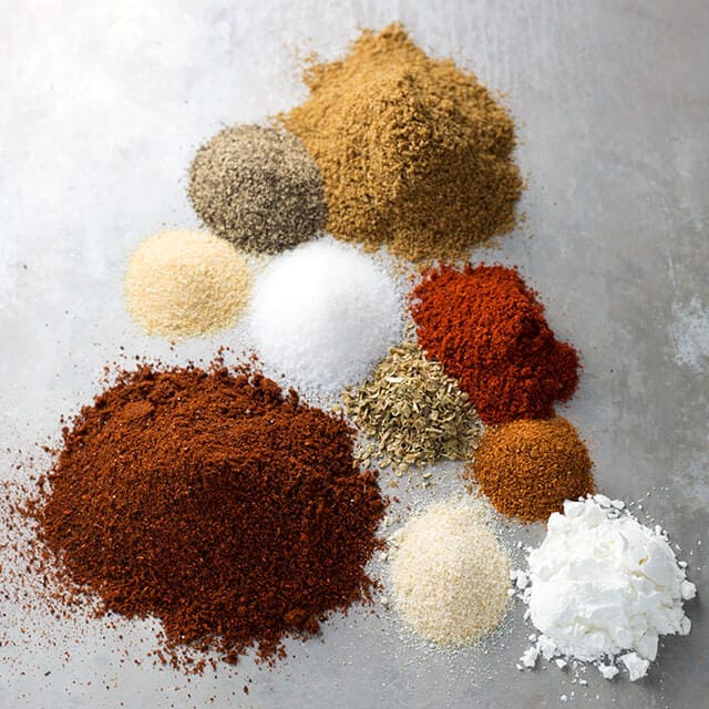 Small mounds of ten different spices on silver background