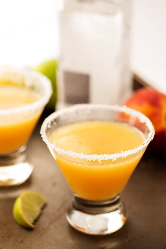 This Fancy Peach Margarita in small glass with salt on the rim on wooden board