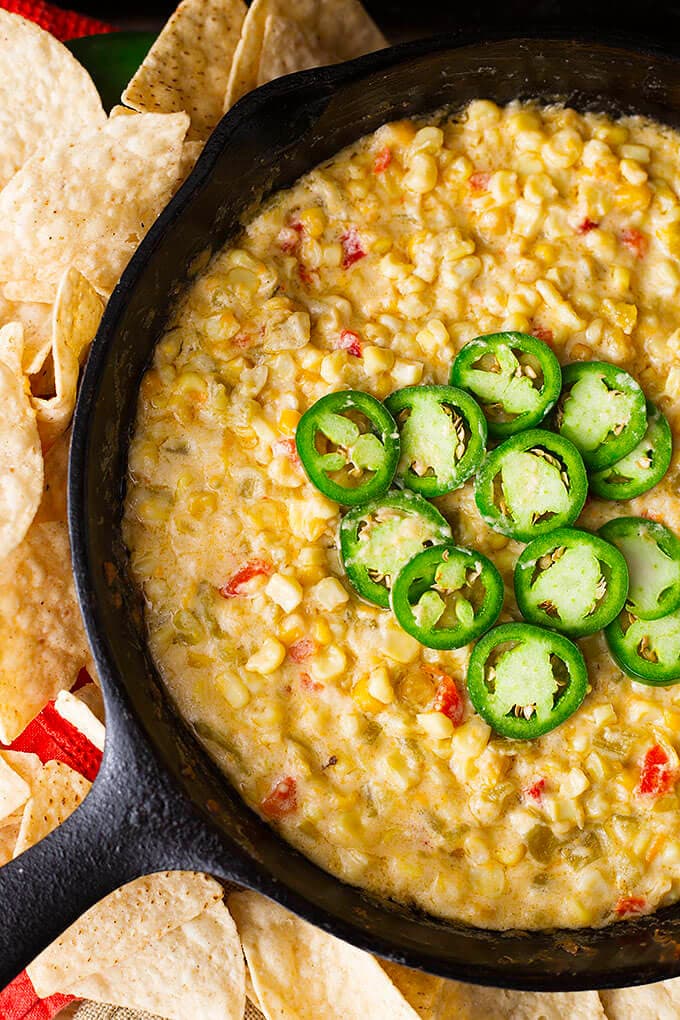 Hot Cheesy Corn Dip in a cast iron skillet topped with jalapenos surrounded by tortilla chips.
