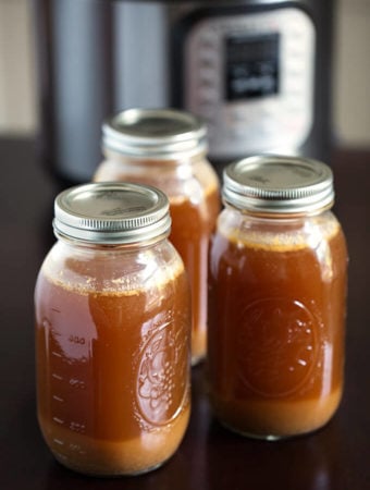 Three jars of Instant Pot Bone Broth with lids on and pressure cooker in the background