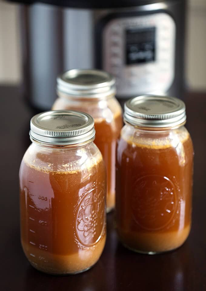 Three jars of Instant Pot Bone Broth with lids on and pressure cooker in the background