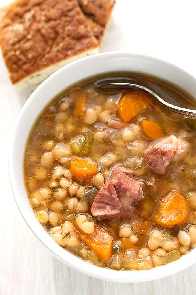 Instant Pot Ham Hock and Bean Soup in white bowl with spoon on white wood background