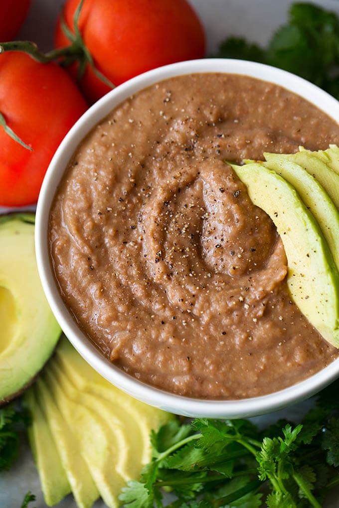 Close up of Refried Beans in small white bowl with sliced avocado