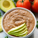 Instant Pot Refried Beans in small white bowl topped with thinly sliced avocado