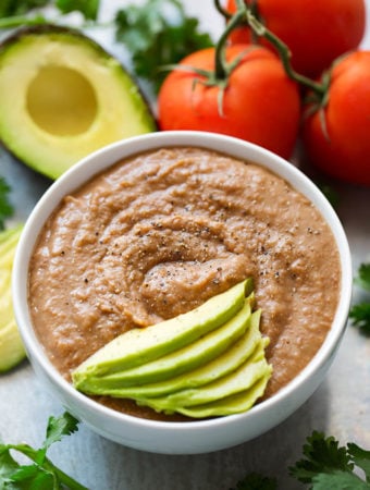 Instant Pot Refried Beans in small white bowl topped with thinly sliced avocado