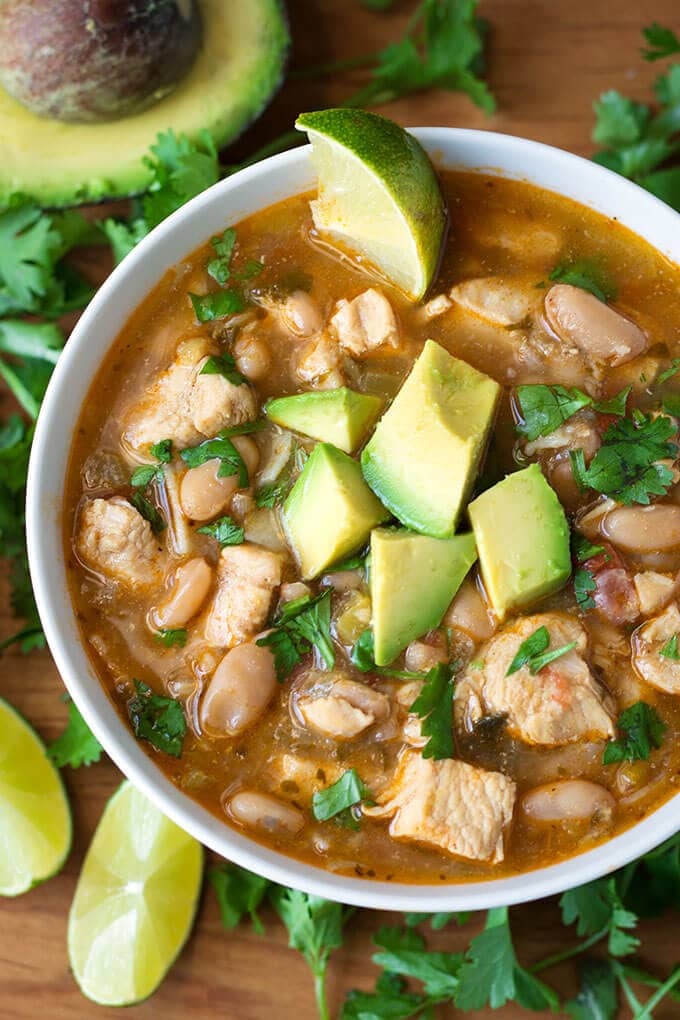 Instant Pot White Chicken Chili in a white bowl topped with avocado surrounded by cilantro leaves and lime slices