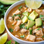Instant Pot White Chicken Chili in a white bowl topped with avocados surrounded by cilantro and lime slices