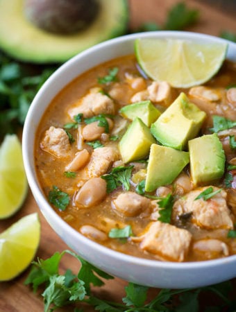 Instant Pot White Chicken Chili in a white bowl topped with avocados surrounded by cilantro and lime slices