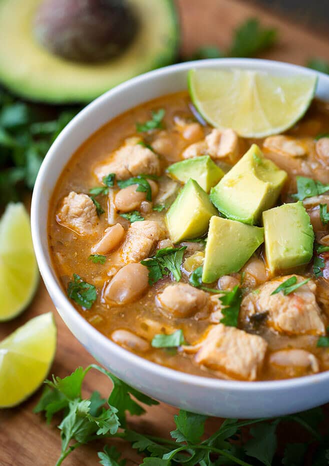 Instant Pot White Chicken Chili in a white bowl topped with avocados surrounded by cilantro and lime slices