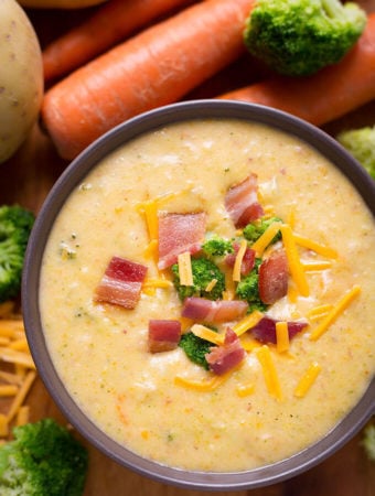 Loaded Broccoli Cheese & Potato Soup in a dark colored bowl with carrots and broccoli in the background