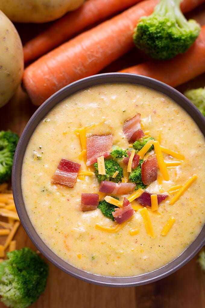 Loaded Broccoli Cheese & Potato Soup in small purple bowl with carrots and broccoli in background