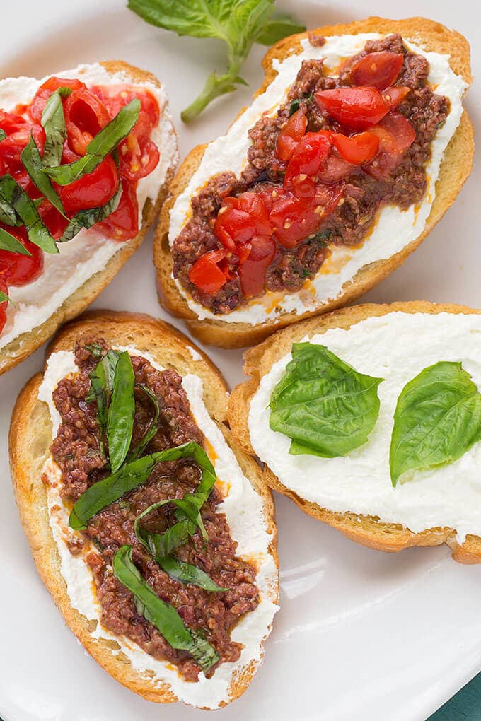 Four pieces of toasted bread with whipped feta spread and Olive Tapenade on white plate