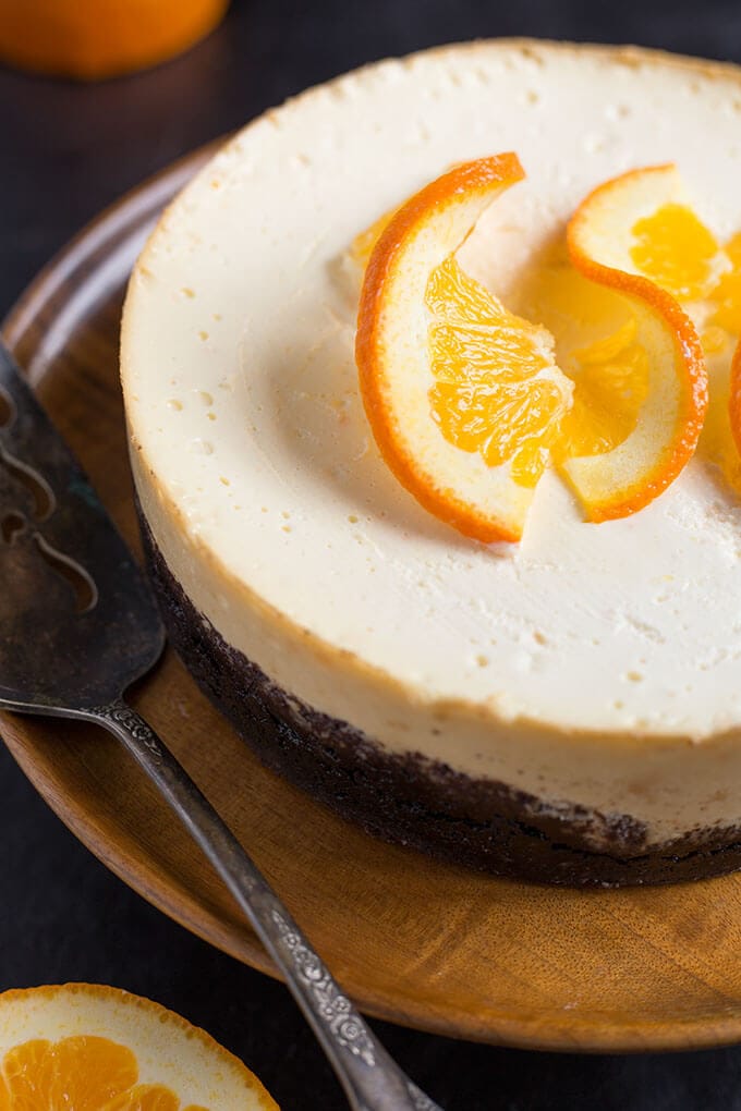 Whole Pressure Cooker Dreamy Orange-Cheesecake on a wooden platter topped with orange