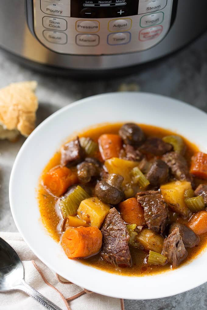 Beef Stew in a white bowl in front of a pressure cooker
