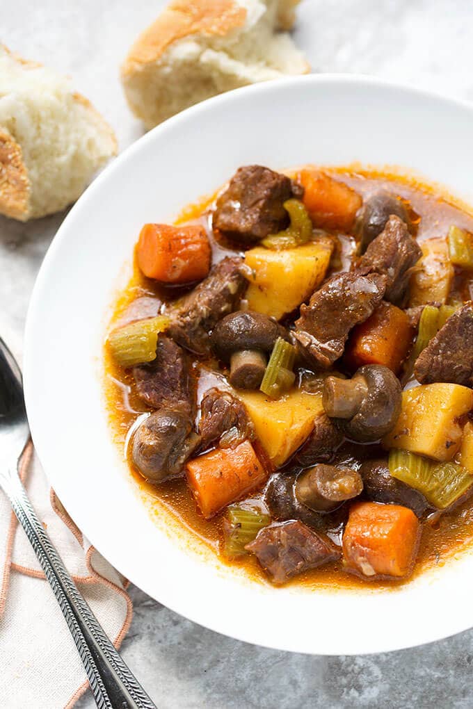 Sandy's Instant Pot Beef Stew in white bowl next to silver spoon and chunks of bread