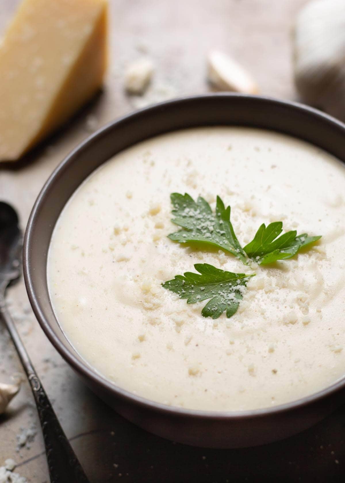 Garlic Parmesan Cream Sauce in a black bowl on a wooden board garnished with parsley