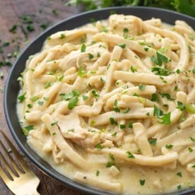 Instant Pot Chicken and Noodles in a black bowl on wooden board next to two golden forks