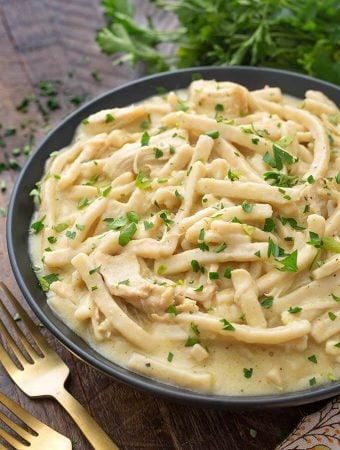 Instant Pot Chicken and Noodles in a black bowl on wooden board next to two golden forks