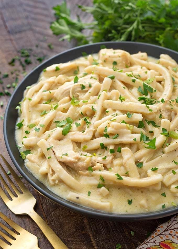 Instant Pot Chicken and Noodles in a shallow black bowl on wooden board next to two golden forks