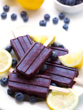 Five Blueberry Lemon Popsicles on a white plate with lemon slices and blueberries