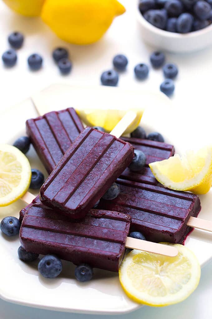 Five Blueberry Lemon Popsicles on a white plate with lemon slices and blueberries