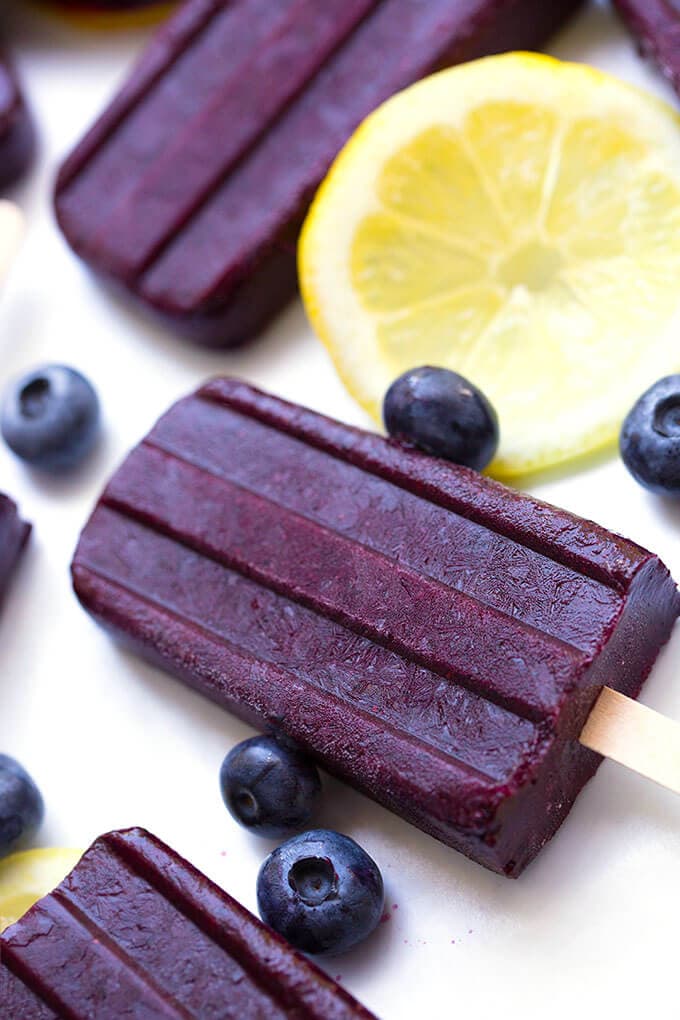 Closeup of Blueberry Lemon Popsicles on a white background with lemon slice and scattered blueberries