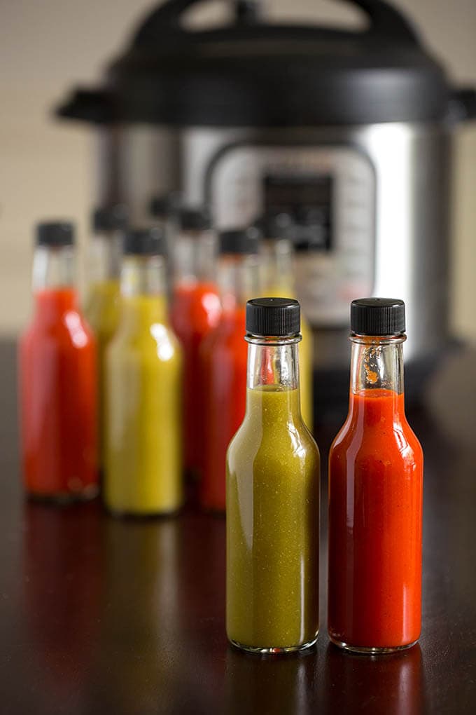  Several green and red glass bottles of hot sauce in front of a pressure cooker