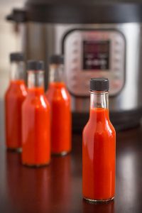 Four bottles of red hot sauce in front of pressure cooker