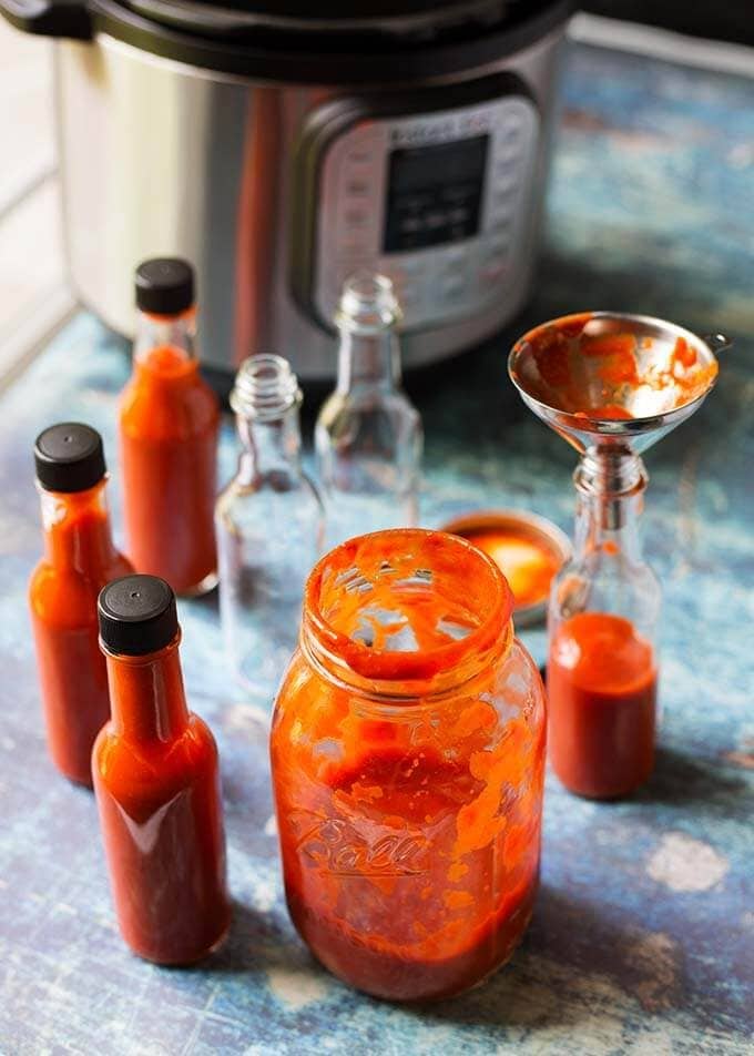 Pouring hot sauce into small glass bottles using a funnel